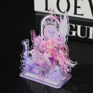 May include: A clear acrylic figurine featuring a female anime character with long pink hair, wings, and a clock design. The figurine has a lavender and pink colour scheme and is on a rectangular base.