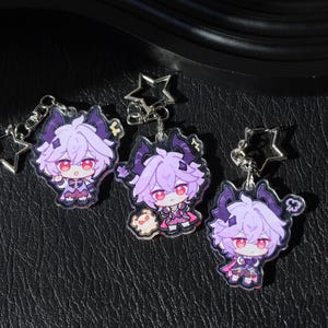 May include: Three anime-style keychains featuring a character with purple hair, red eyes, and dark horns. The keychains are attached to silver star-shaped clasps. The character is wearing a pink and purple outfit.