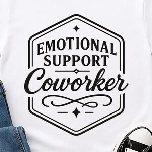 May include: White t-shirt with the text "EMOTIONAL SUPPORT Coworker" in a black, decorative design. The shirt is paired with blue jeans and black canvas sneakers with white laces.