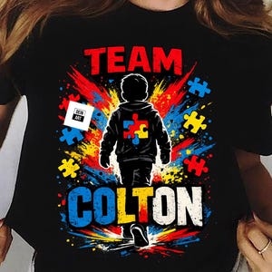 Pode incluir: Camiseta preta com as palavras "TEAM COLTON" em vermelho e branco. A camiseta apresenta um gráfico de uma criança com um design de peça de quebra-cabeça nas costas, cercada por peças de quebra-cabeça coloridas.