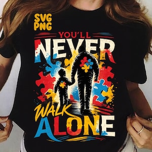 May include: Black t-shirt with the words "YOU'LL NEVER WALK ALONE" in white, red, and yellow. The design features two figures holding hands, with puzzle piece accents in blue, red, and yellow. The top left corner has the words "SVG PNG".