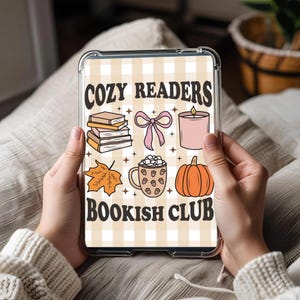Op de afbeelding: Een doorzichtige tablethoes met een ontwerp met de tekst "COZY READERS BOOKISH CLUB". Het ontwerp bevat illustraties van boeken, een strik, een kaars, een blad, een mok cacao en een pompoen.