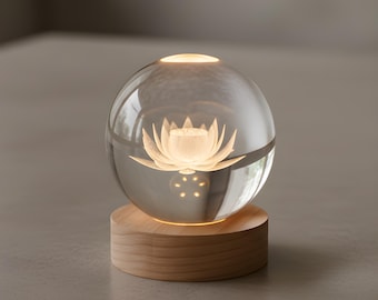 以下が含まれることがあります： 丸い木製の台座の上に置かれた、照明付きの蓮の花のデザインが施された透明なガラス球。 球体の上部にはライトがあり、台座は明るい色の木材で作られています。 全体的な効果は、暖かく輝く装飾品です。