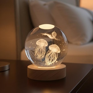 May include: A clear glass sphere lamp with two jellyfish designs and a wooden base. The lamp emits a soft glow, creating a calming ambiance. The jellyfish are intricately detailed, adding a touch of marine life to the decor.