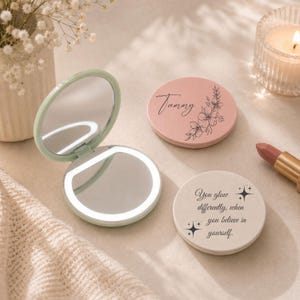 May include: A round, light green compact mirror with an integrated LED light ring. Two additional circular compact mirrors are present: one dusty pink with the name Tammy and a floral design, and one cream with the text You glow differently, when you believe in yourself.
