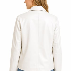 May include: A cream-coloured blazer with long sleeves and a collared neckline. The jacket is paired with blue jeans. The back view of the jacket shows a tailored fit. The blazer is made of a smooth, possibly leather-like material.
