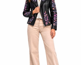 May include: A black leather motorcycle jacket featuring colourful floral embroidery on the lapels and sleeves, worn over a white crochet top and light beige wide-leg trousers, paired with white trainers.