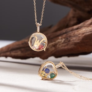 Può includere: Due collane color oro con pendenti trasparenti, rotondi e a forma di cuore. Il pendente rotondo contiene la lettera "W" e gemme colorate. Il pendente a forma di cuore contiene anche gemme colorate. Entrambi i pendenti pendono da delicate catene d'oro.