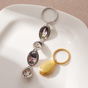 May include: Two keychains, one silver and one gold, displayed on a white surface. The silver keychain features a series of oval-shaped lockets, each holding a small photograph. The gold keychain has a single, oval locket with a floral design.