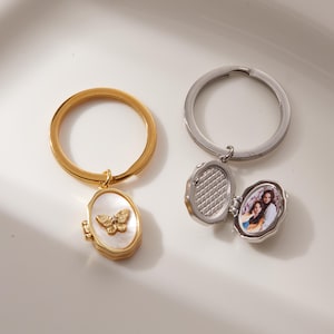 May include: Two keyrings. One gold-coloured with a butterfly pendant and a mother-of-pearl background. The other is silver-coloured, with an oval locket that opens to reveal a photo. Both have round key rings.