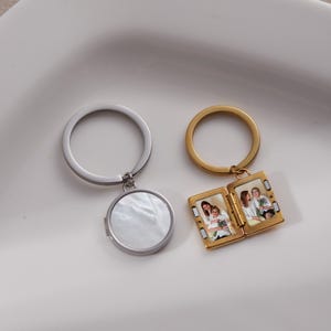 Puede incluir: Dos llaveros. Uno es plateado con un colgante redondo con un diseño de nácar. El otro es dorado y se abre para revelar dos pequeños marcos de fotos. Cada marco contiene una fotografía en color de personas.