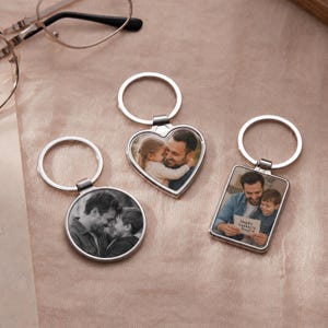 May include: Three silver-toned metal keychains featuring custom photo inserts. One is circular, one is heart-shaped, and one is rectangular. The rectangular keychain displays a photo with the text Happy Father's Day! and a small red heart icon.