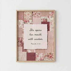 Puede incluir: Un cuadro decorativo con un collage de cuadrados de tela rosa y blanca con patrones florales, de cuadros vichy y de rayas. En el centro, un papel rosa claro con bordes irregulares muestra el texto en negro: She opens her mouth with wisdom. Proverbs 31:26.