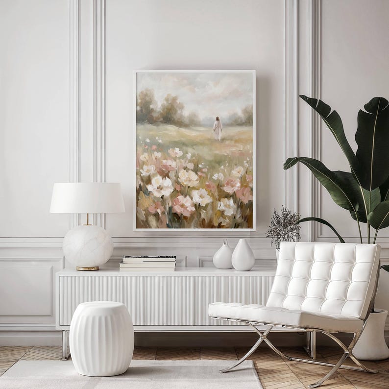 May include: A framed floral landscape painting with a white border. The artwork depicts a field of white and pink flowers with a figure walking in the distance. The painting is displayed above a white cabinet with a lamp and decorative items.