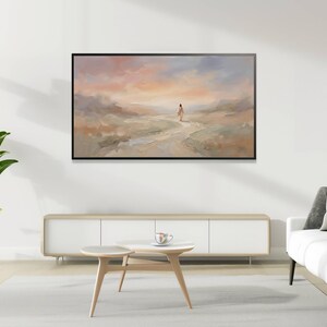 K&ouml;nnte beinhalten: Abstrakte Landschaftsmalerei in einem schwarzen Rahmen. Das Kunstwerk zeigt eine Figur, die auf einem Pfad geht, mit einer sanften Farbpalette aus Pfirsich, Blau und Beige. Das Gem&auml;lde h&auml;ngt &uuml;ber einem wei&szlig;en Schrank und einem hellfarbigen Teppich.