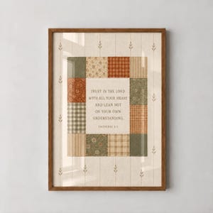 May include: A framed wall art print featuring a central white panel with the text Trust in the Lord with all your heart and lean not on your own understanding. Proverbs 3:5, surrounded by a patchwork border of green, tan, and orange fabric patterns.