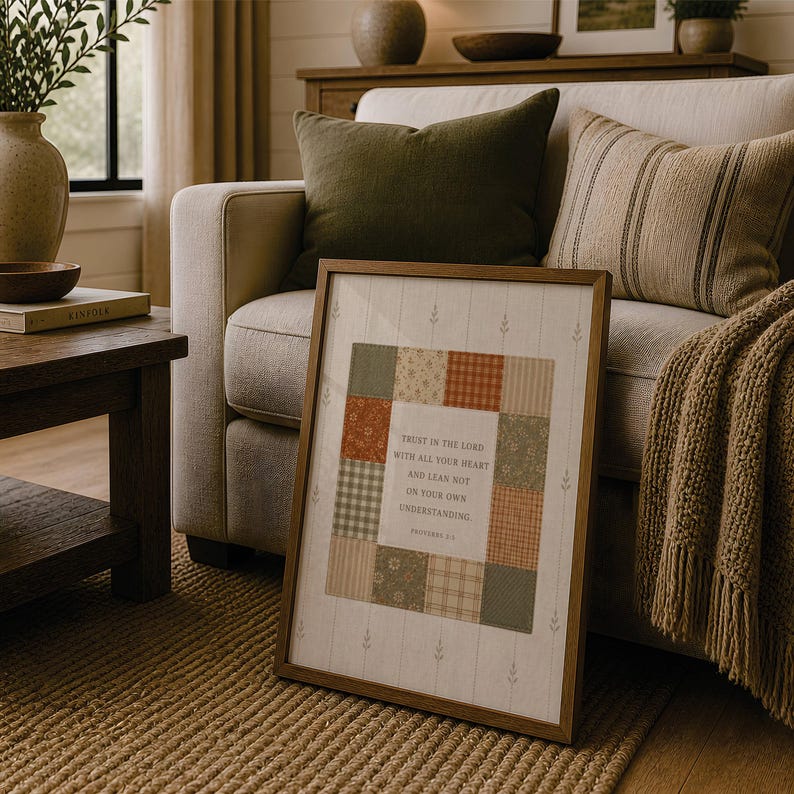 May include: A framed wall art piece featuring a central square composed of various fabric-like patches in shades of green, orange, and beige. The text reads: Trust in the Lord with all your heart and lean not on your own understanding. Proverbs 3:5.