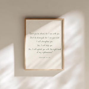 Puede incluir: Una pieza de arte mural rectangular enmarcada con un fondo beige claro y texto en negro que dice: "Don't you be afraid, for I am with you. Don't be dismayed, for I am your God. I will strengthen you. Yes, I will help you. Yes, I will uphold you with the right hand of my righteousness." y "ISAIAH 41:10" en la parte inferior.