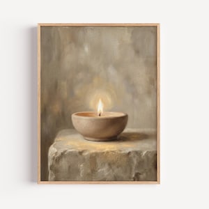 May include: A framed oil painting depicting a small, round, beige ceramic bowl containing a lit candle with a warm, glowing flame. The bowl rests on a textured, light-coloured stone surface against a soft, neutral-toned, painterly background.