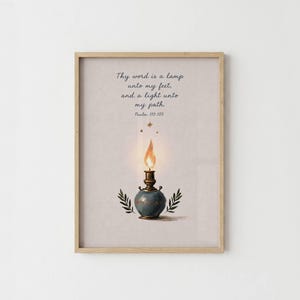 May include: A framed wall art print featuring a light blue oil lamp with a glowing orange flame. Above the lamp, the text reads: Thy word is a lamp unto my feet, and a light unto my path. Psalm 119:105. Two green leafy sprigs flank the lamp base.