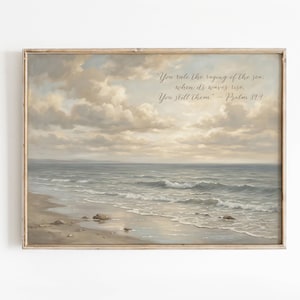 May include: A framed landscape print depicts a serene beach scene with a cloudy sky and ocean waves. The artwork features a muted color palette of beige, gray, and blue. Text on the print reads: "You rule the raging of the sea: when its waves rise, You still them" - Psalm 89:9.