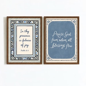 May include: Two framed wall art prints with dark wood frames. The left print features a cream background with blue striped borders, a floral frame, and the text In thy presence is fulness of joy. Psalm 16:11. The right print has a blue background.