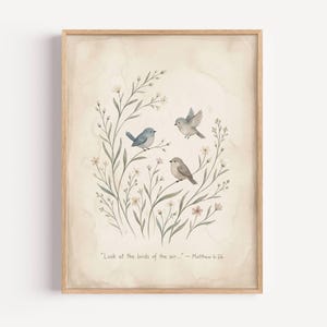 Op de afbeelding: Een ingelijste aquarelprint met drie kleine vogels die tussen delicate bloemtakken zitten. De vogels zijn in tinten blauw en bruin, tegen een zachte, beige achtergrond. De quote "Kijk naar de vogels in de lucht..." staat onderaan afgedrukt.