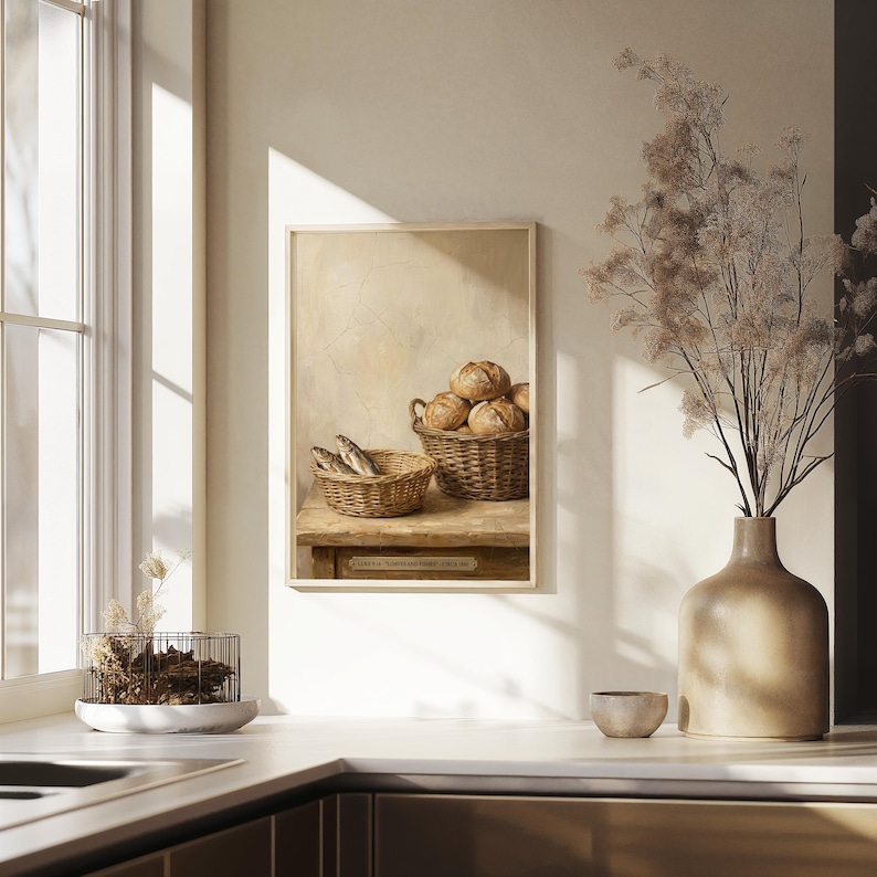 May include: A framed painting depicts two wicker baskets, one with fish and the other with round loaves of bread. The painting is in a warm, neutral color palette, with a rustic, vintage aesthetic. The painting is displayed on a wooden table.