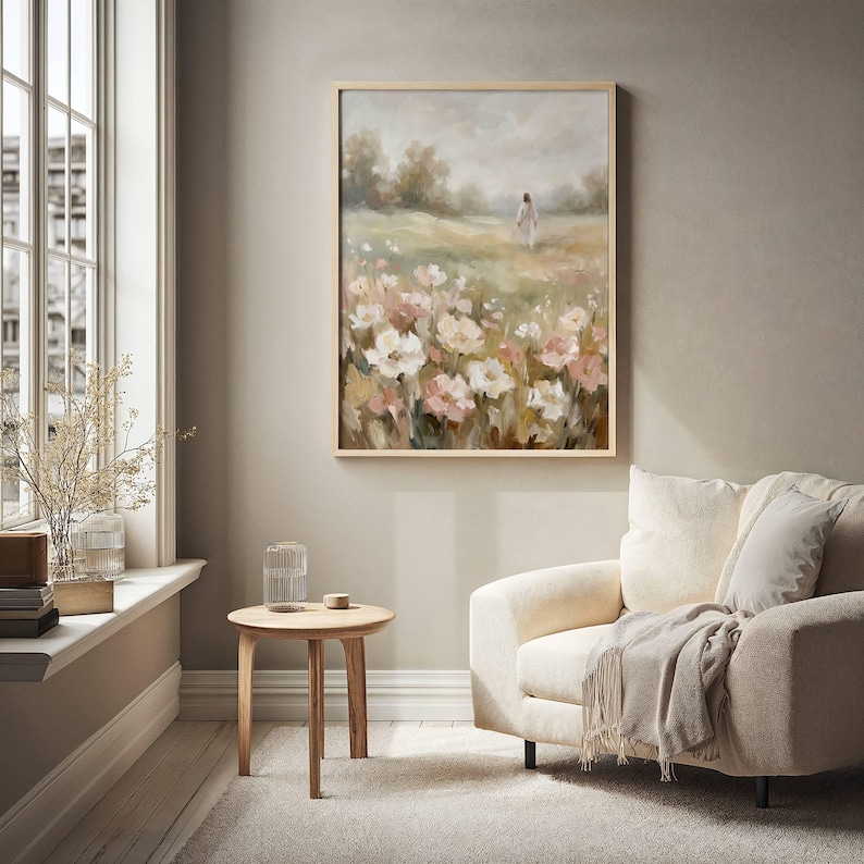 May include: A framed painting depicts a figure walking in a field of flowers. The artwork features a soft color palette of pink, white, and green, with a light brown wooden frame. The painting hangs above a cream-colored armchair.
