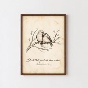 Puede incluir: Una lámina de arte enmarcada sobre papel crema envejecido con una ilustración en tinta negra de dos pájaros posados juntos en una rama. Debajo de los pájaros, el texto dice: Let all that you do be done in love. 1 Corinthians 16:14.
