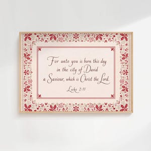 May include: A rectangular framed wall art piece featuring a cream-coloured centre with the text For unto you is born this day in the city of David a Saviour, which is Christ the Lord. Luke 2:11. The border displays red holly and snowflake motifs.