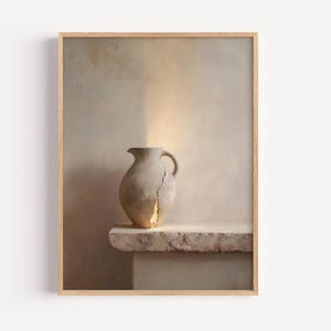May include: A framed print featuring a still life of a beige ceramic jug with a handle, resting on a stone ledge. The jug has a visible crack filled with gold. The background is a neutral beige.