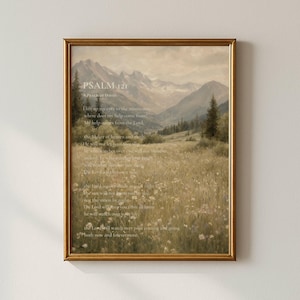 May include: A framed wall art print featuring a landscape painting of a mountain range and a wildflower meadow. The text of Psalm 121 is overlaid in white lettering across the center of the image, set within a thin, metallic gold frame.