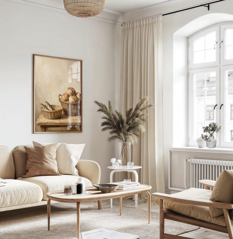 May include: A cozy living room scene with a beige sofa, wooden coffee table, and a framed artwork. The artwork depicts a still life of bread and fish in baskets. A large window with cream-colored curtains provides natural light.