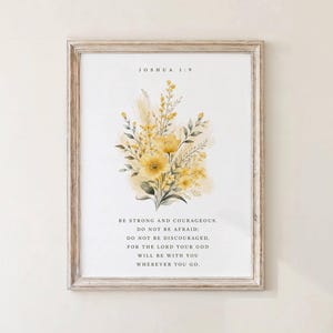 May include: A framed print featuring a watercolor floral arrangement in shades of yellow and green. The print includes the text "JOSHUA 1:9" and an inspirational quote about courage and faith. The frame is a light, natural wood.