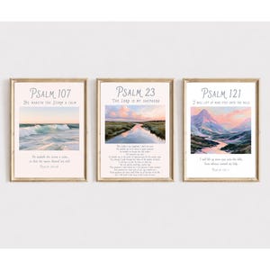 Op de afbeelding: Drie ingelijste wandkunstprints met bijbelverzen. De linker print toont Psalm 107 met een oceaanlandschap. De middelste print toont Psalm 23 met een moeraslandschap. De rechter print toont Psalm 121 met een berglandschap. Elke print heeft een licht houten lijst.