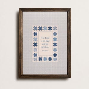 Op de afbeelding: Een ingelijste kunstdruk met een lichtblauwe en witte gingham-achtergrond. Het midden toont een crèmekleurige rechthoek omrand door blauwe stervormige quiltpatronen, met de tekst: The Lord is my light and my salvation. Psalm 27:1.