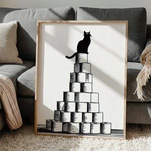 Könnte beinhalten: Ein gerahmter Kunstdruck mit einer schwarzen Katze auf einer Pyramide aus Toilettenpapierrollen. Die Illustration ist in Schwarzweiß gehalten und hat einen minimalistischen Stil. Der Rahmen ist helles Holz, und das Kunstwerk befindet sich auf weißem Hintergrund.