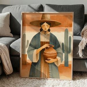 May include: Watercolor print of a person in a wide-brimmed hat and blue robe holding a brown pot. The artwork features a desert landscape with cacti and a warm color palette of orange, brown, and blue. The framed art is displayed indoors.
