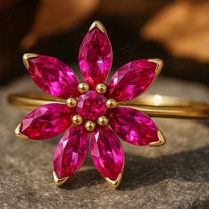 May include: A gold ring featuring a flower-shaped cluster of six marquise-cut vibrant pink gemstones surrounding a central round pink gemstone. The petals are arranged in a symmetrical floral pattern, set on a thin, polished gold band.