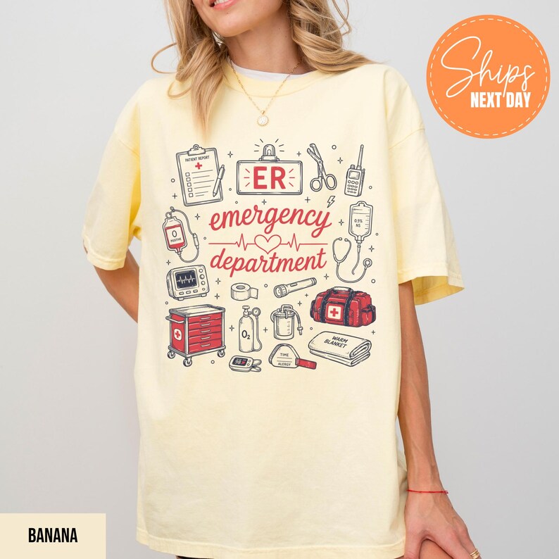 Puede incluir: Una camiseta de color amarillo p&aacute;lido con un estampado gr&aacute;fico que incluye el texto "ER emergency department" en rojo. El dise&ntilde;o presenta varias ilustraciones m&eacute;dicas como un portapapeles, tijeras, un coraz&oacute;n, un monitor y un botiqu&iacute;n.