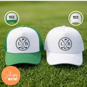 May include: Two trucker hats featuring a white front panel and a circular logo with the letters L and B, crossed golf clubs, and a golf ball. One hat has a green mesh back and brim, while the other is entirely white with a white mesh back.