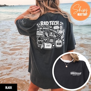 May include: Black t-shirt with a white graphic on the back that says "RAD TECH" with medical-themed illustrations and text. The front of the shirt has the word "RADIOLOGY" printed in white. The shirt is worn by a person on a beach.