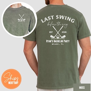 May include: A moss green t-shirt featuring white graphics. The back displays crossed golf clubs, a golf ball, and the text "LAST SWING before the ring EST 2026 RYAN'S BACHELOR PARTY MIAMI, FL". The front chest area shows a smaller crossed golf club logo.