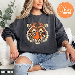 A woman wearing a gray sweatshirt with a tiger graphic is sitting on a couch.