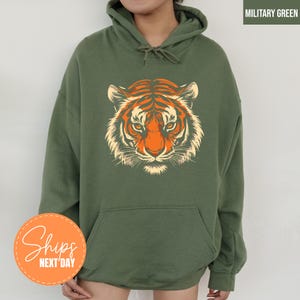 A person wearing a green hoodie with a graphic of a tiger's face printed on it.