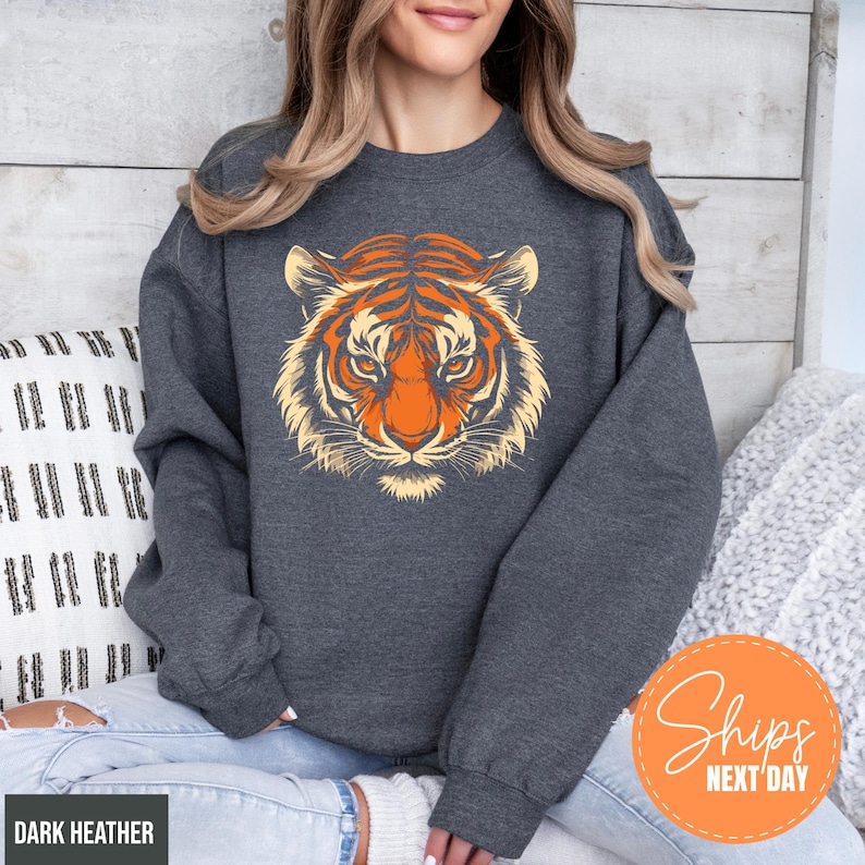 A woman wearing a gray sweatshirt with a tiger graphic on it, sitting on a couch.