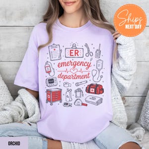 Puede incluir: Una camiseta de color morado claro con un estampado gr&aacute;fico de equipo m&eacute;dico de urgencias en tinta roja y negra. El dise&ntilde;o incluye ilustraciones de un informe de paciente, tijeras, una radio, una bolsa de suero, un monitor card&iacute;aco y un botiqu&iacute;n.