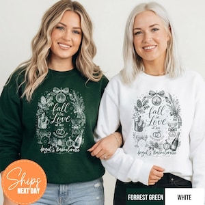 May include: A dark green sweatshirt and a white sweatshirt, each featuring a graphic print with the text "fall in Love est 2027" and "Angel's Bachelorette" surrounded by illustrations of a disco ball, pinecones, drinks, and wedding rings.