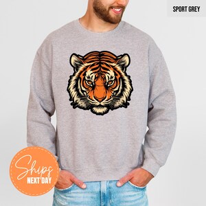 A man wearing a grey sweatshirt with a graphic of a tiger's head printed on it.
